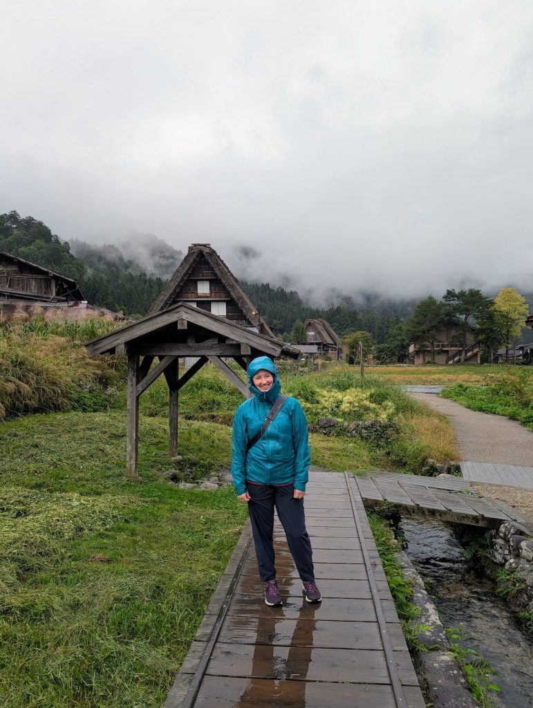 A woman in a teal rain jacket standing in the rain in a traditional Japanese village