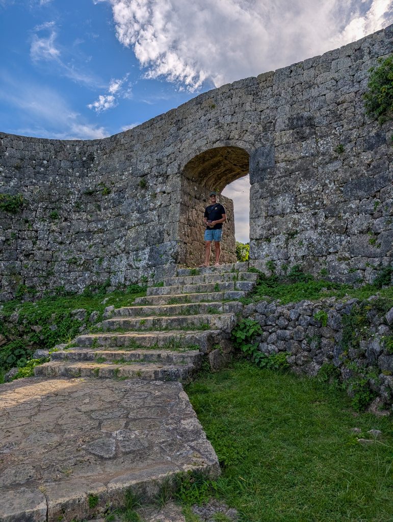 A man standing in an archway in a stone wall with steps leading down towards the camera.