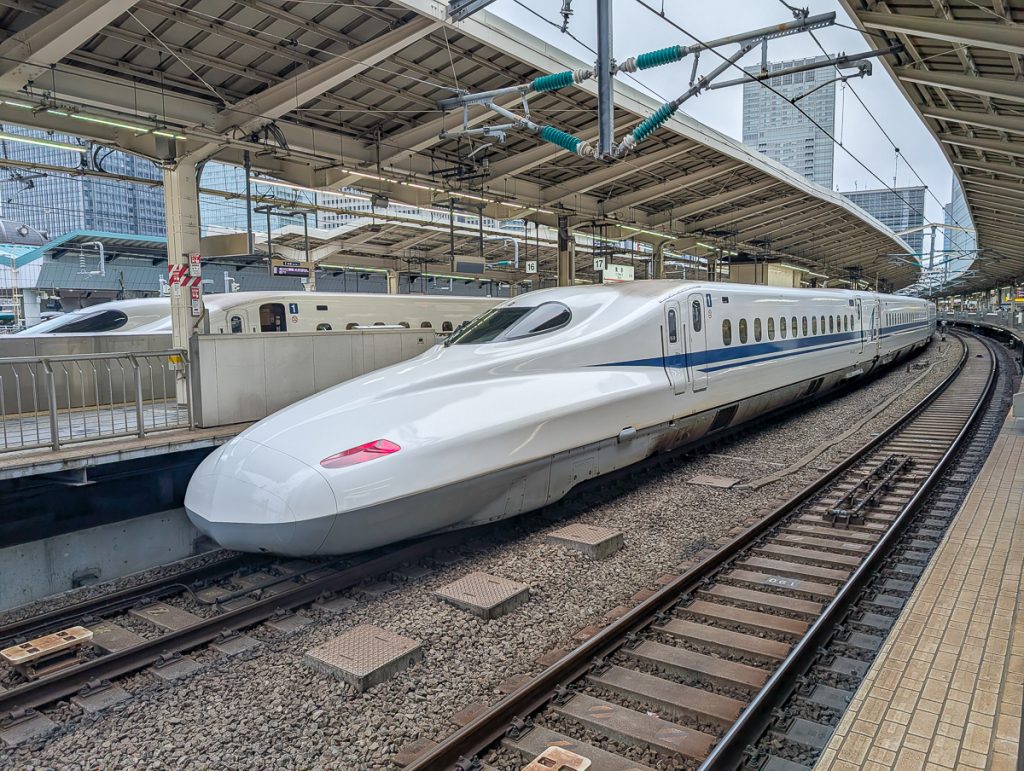 The front of a white Japanese bullet train parked at a train station in a city.