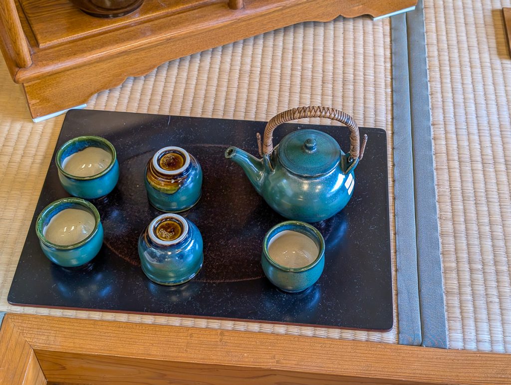An artisanal blue clay teapot and cups set on a black tray.