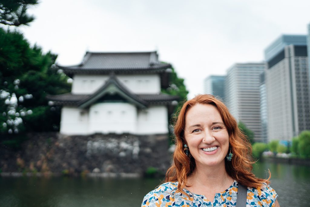 Sooz smiling at the camera with a Japanese temple and office buildings out of focus behind her.