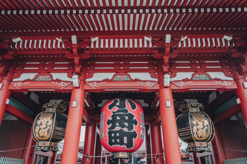 A close up of the red and white architecture and large paper lanterns at a Buddhist temple in Tokyo.