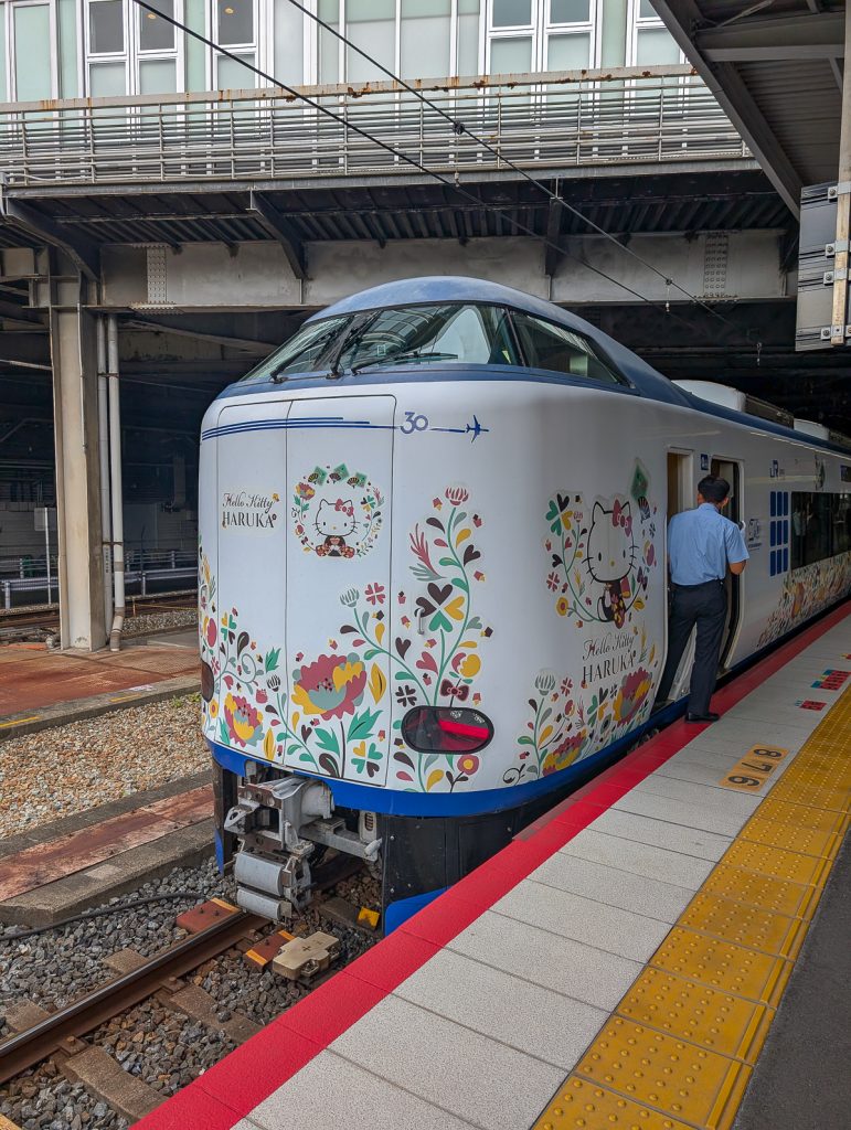 The end of a train at a platform decorated with colorful flowers and Hello Kitty with text saying "Hello Kitty Haruka."