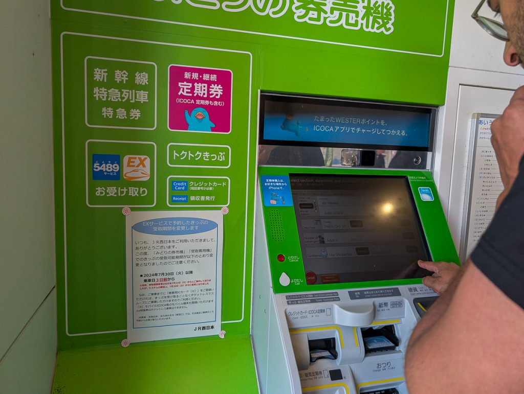 A man using a green transport ticket machine with all the information on it written in Japanese.