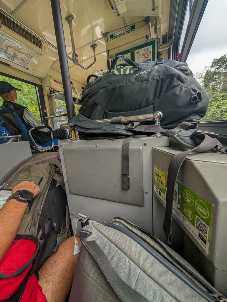 A man's arm and leg on a bag, with more bags packed around, on a bus.