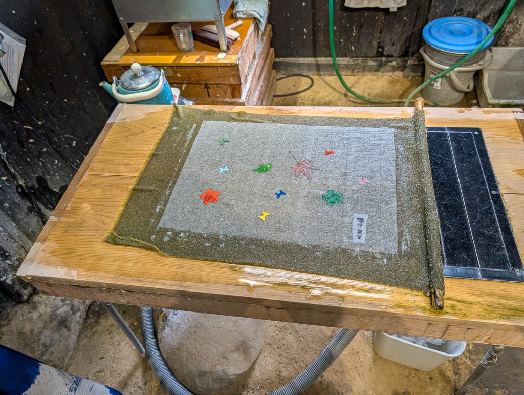 A roll of washi paper being made on a table with small flowers and leaves on the wet paper.