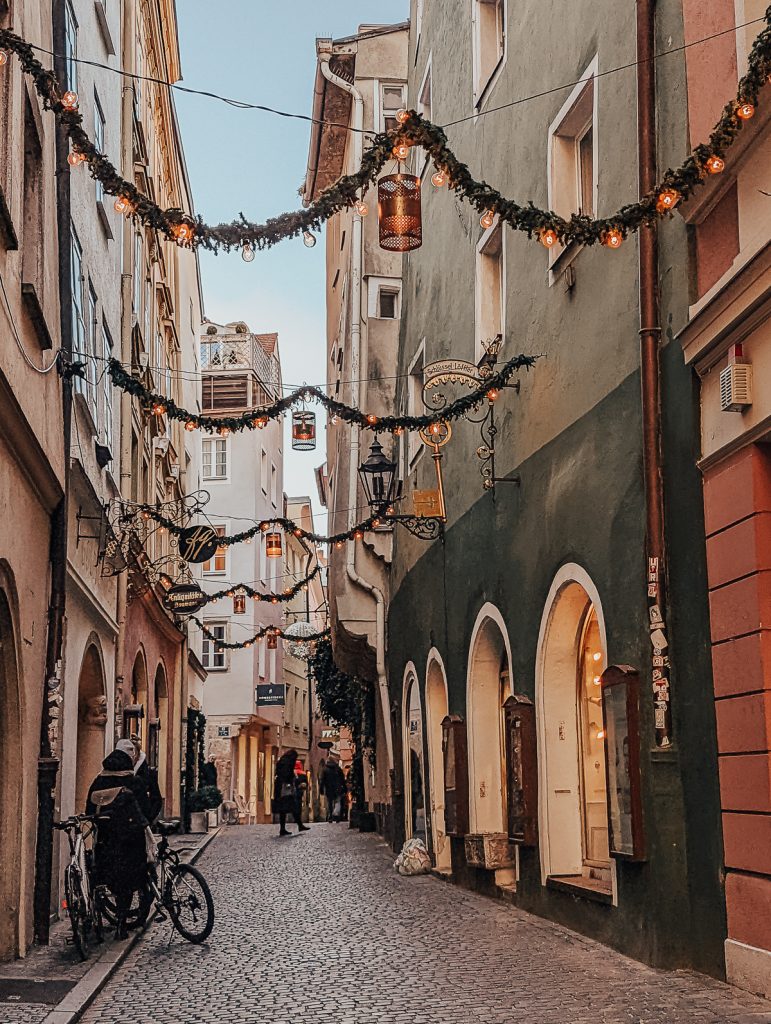 A narrow street in Regensburgh with Christmas decorations strung between buildings.