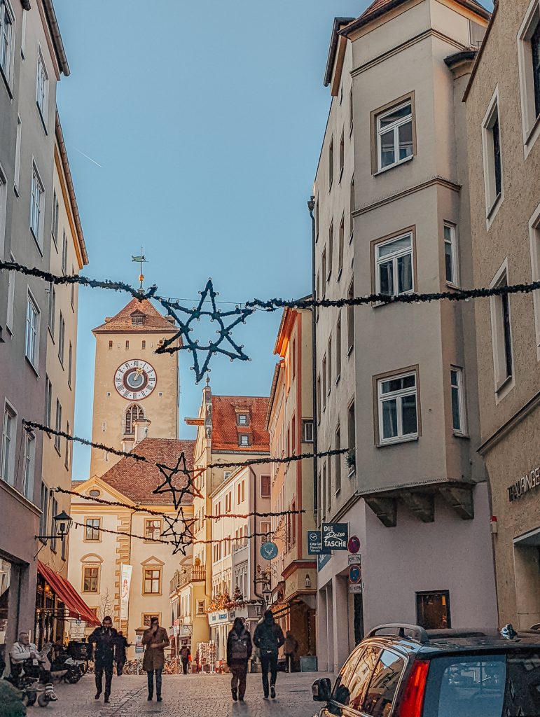 A street in Regensburg leading towards a clock tower with Christmas star decorations strung between the buildings.