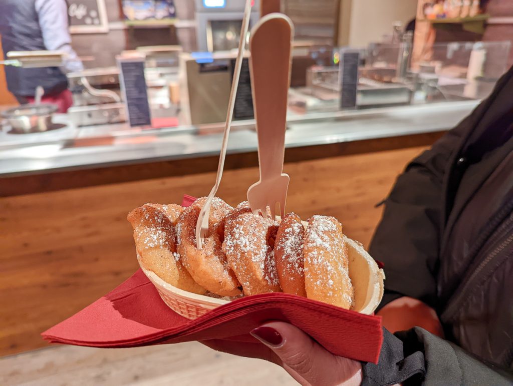 A hand with red nail polish holding a bowl with some kind of fritters with forks standing in them.