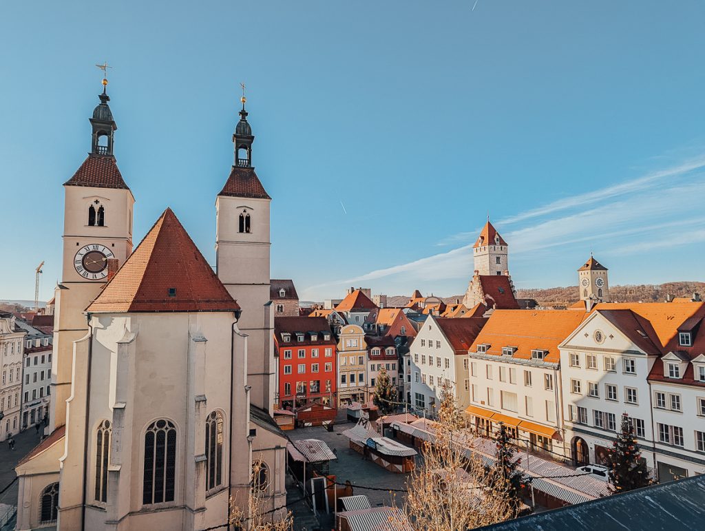 A rooftop view over a city square net to a church with a blue sky above.