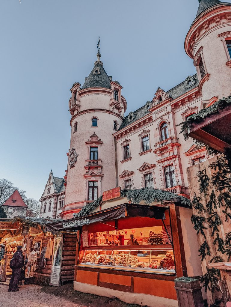 A Christmas food stall in front of a round tower section of a palatial building.
