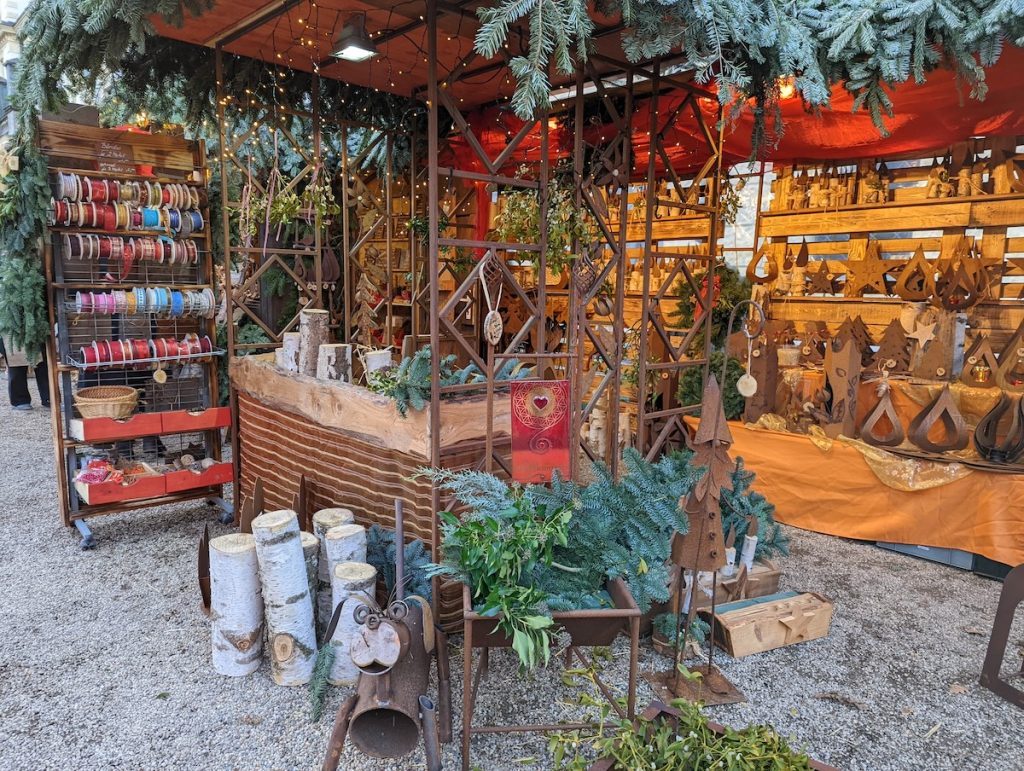 A sustainable stall at Regensburg Christmas Market with spools of ribbon, wooden logs, greenery and sculptures made from metal.