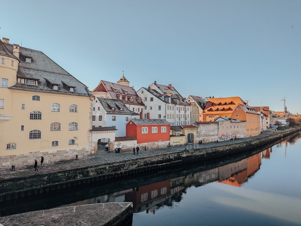 Pastel colored buildings next to the Danube River in Regensburg on a clear day with no clouds.