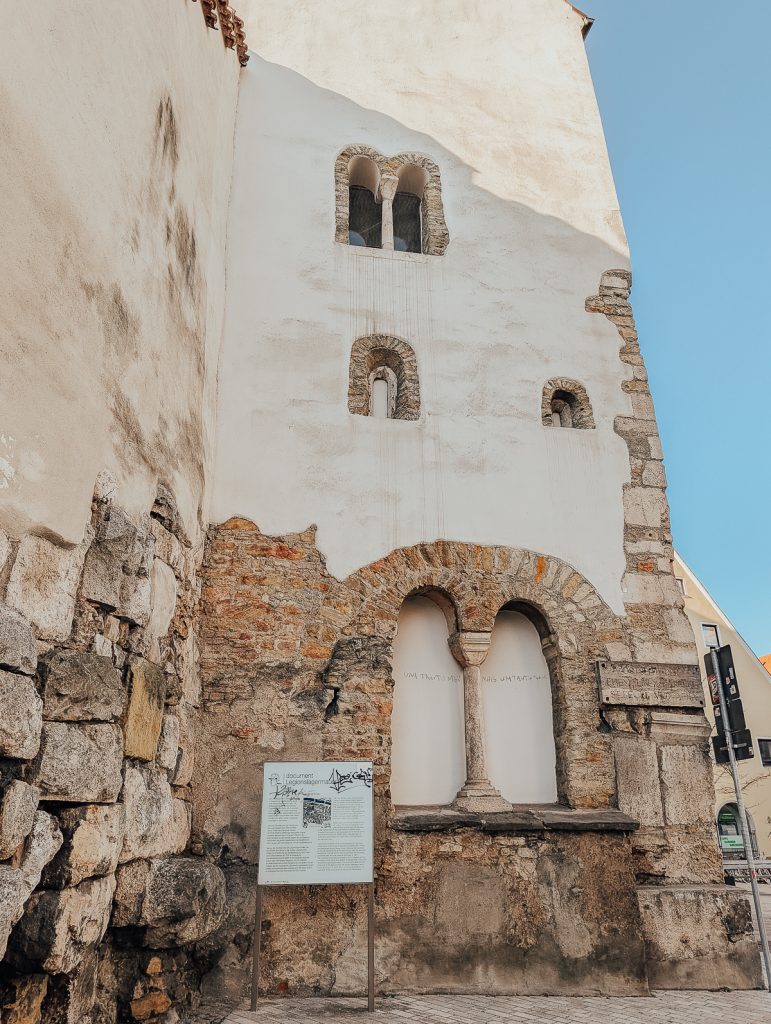 A building showing old foundations with an information board in front of it.
