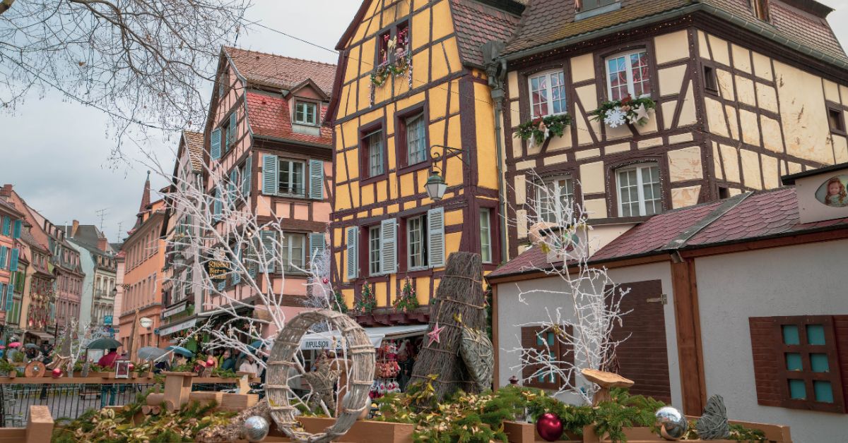A Christmas display made of natural materials in front of colorful timber houses on a gray day.