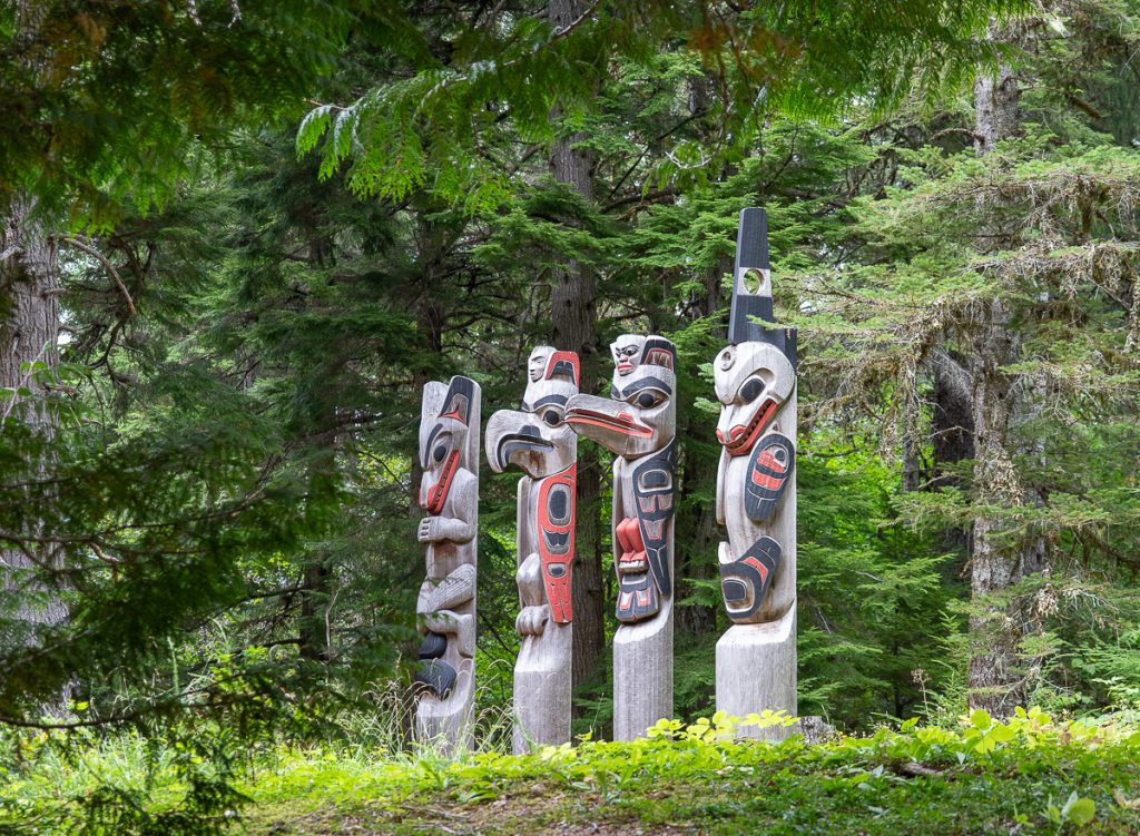 Four carved wooden totem poles standing together surrounded by greenery.