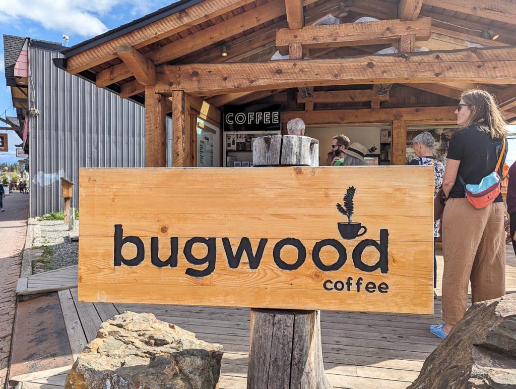 A small wooden building with people lining up and a wooden sign at the front that says "bugwood coffee."