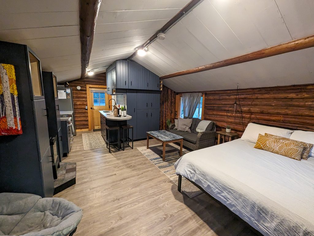 A cozy cabin with an open plan containing a small kitchen, seating area and bed.