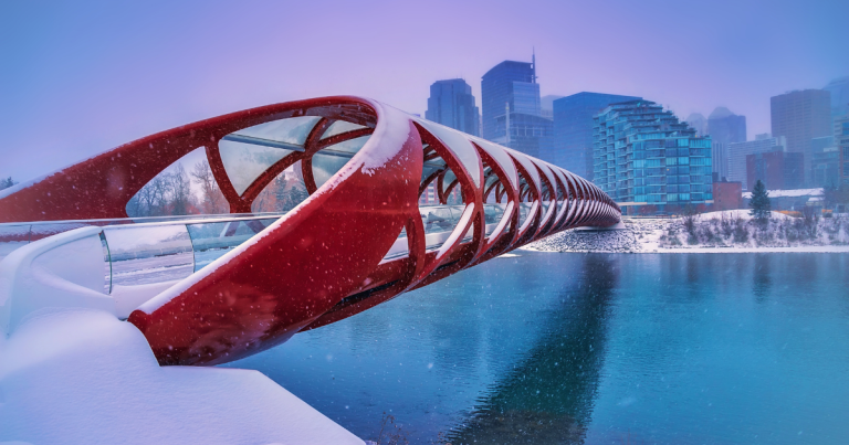 Things to do in Calgary in winter. A red bridge covered in snow over an icy river and snow-filled river bank