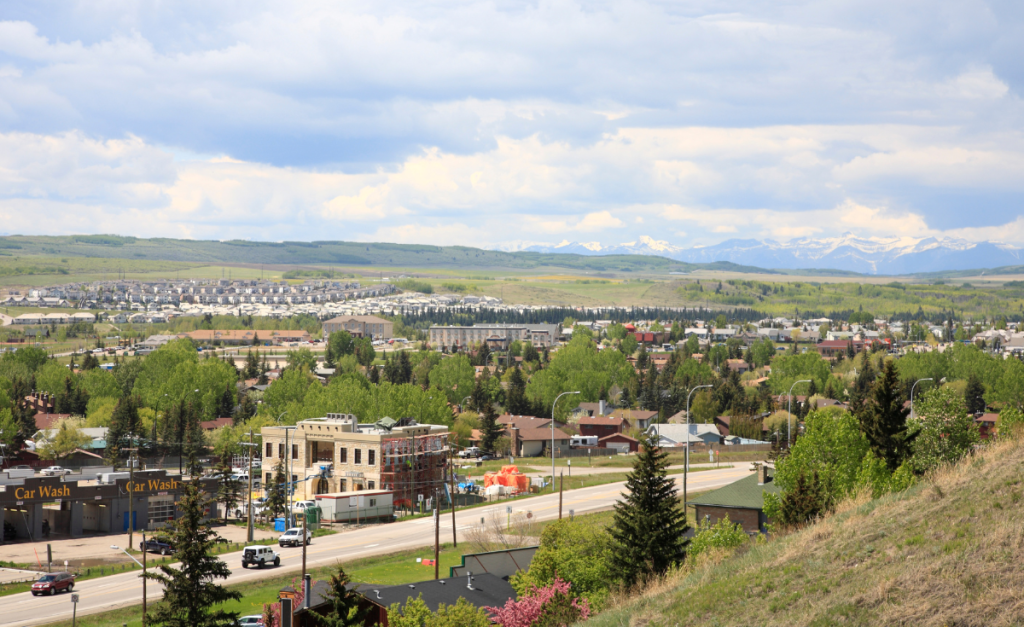 A small-ish city seen from a slight hill with lots of trees around and green rolling hills in the background.
