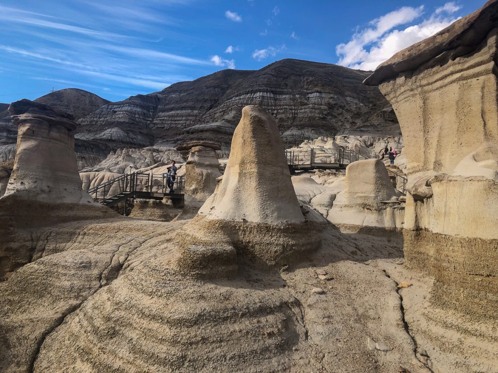 Strange, tower-like rock formations with a walkway and steps plus hills and blue sky in the background.