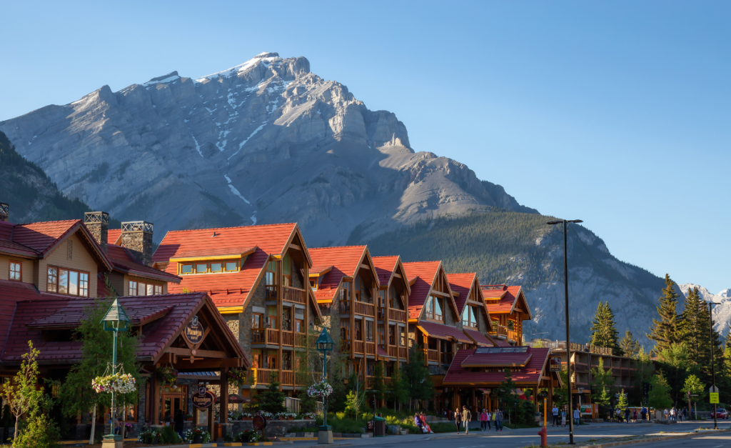 A street of wooden buildings with red roofs with a big rocky mountain and blue sky in the background.