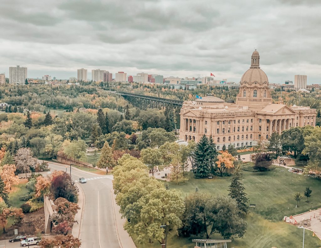 Overhead view of a domed building surrounded by parkland with a road next to it and city buildings in the distance.