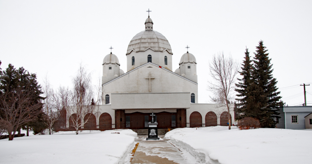 A large white church with three domes on top surrounded by snow.