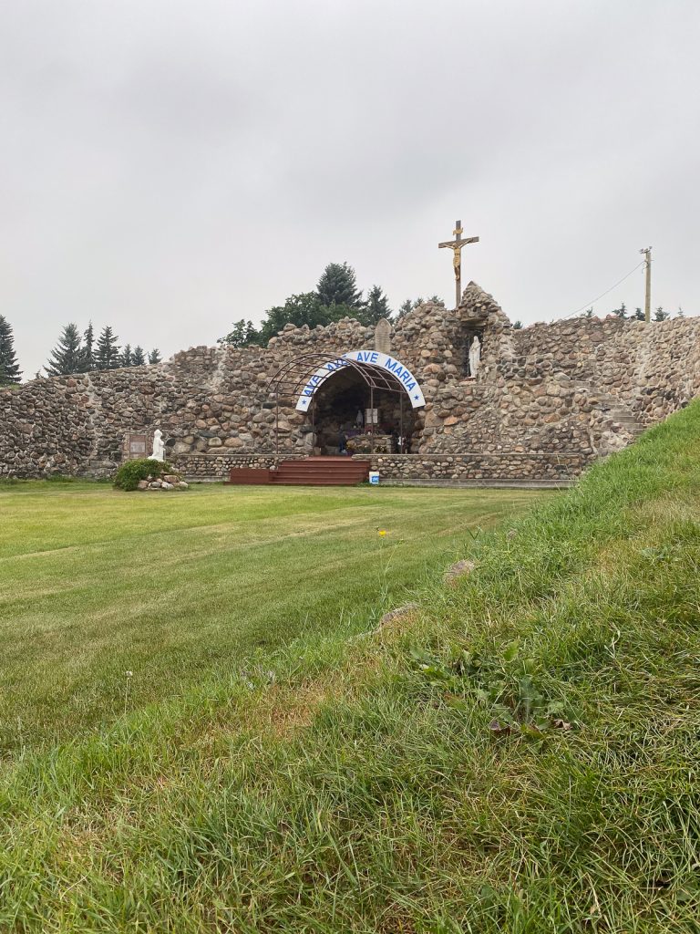 A shrine made completely of rocks with a sign saying "Ave Ave Ave Maria" over the entrance and Jesus on a wooden cross rising above.