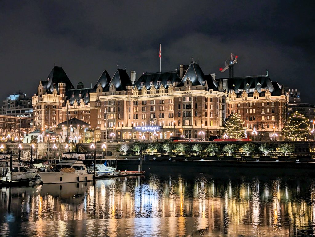 The Fairmont Empress Hotel in Victoria as seen at night from the water with yachts moored in the harbor in front of the hotel.