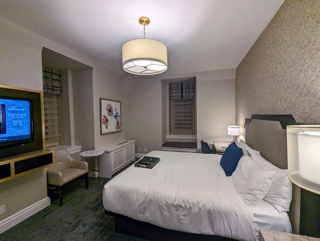A spacious hotel room at night, with a TV on the wall that says Fairmont.