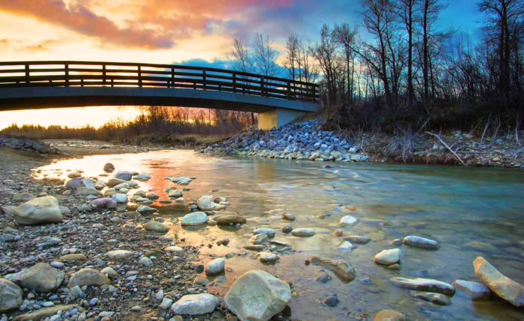 Fish Creek Provincial Park Alberta. A bridge over a rocky stream with a vivid sunset.