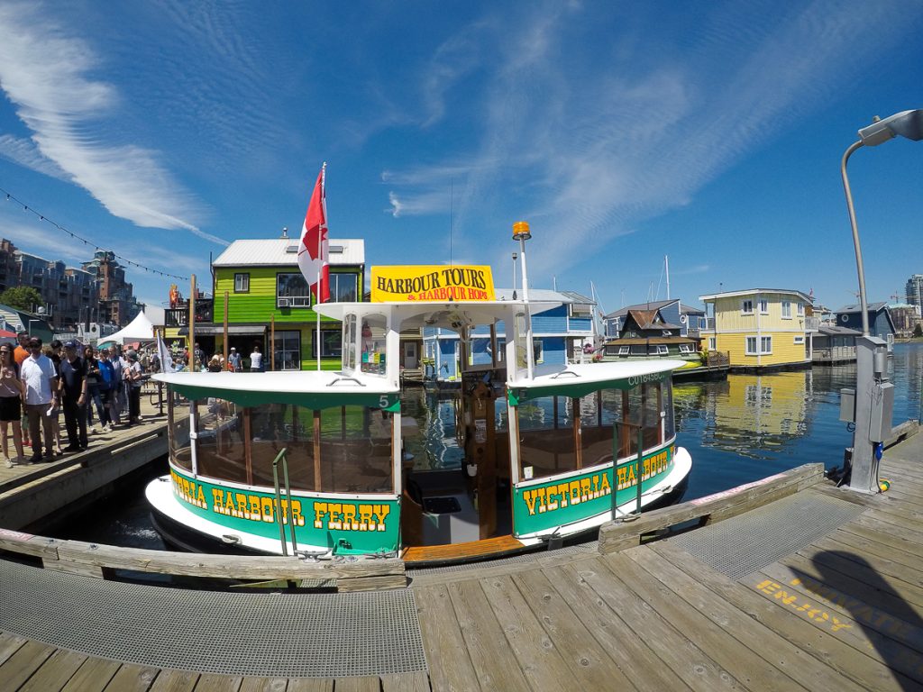 A small Victoria Harbour Ferry moored at a jetty on a sunny day with blue skies above and people lining up to the left of the boat.