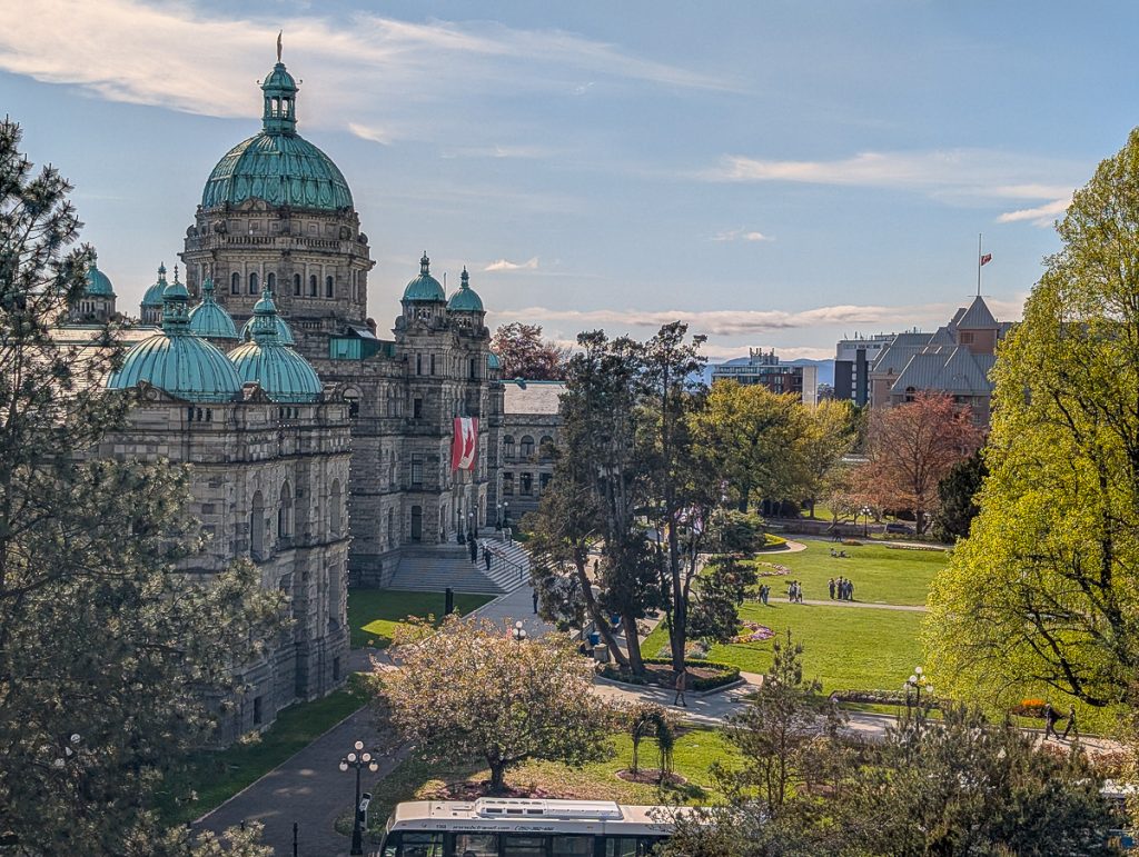 A grand stone building with domed roofs looking over a park area on a sunny day.
