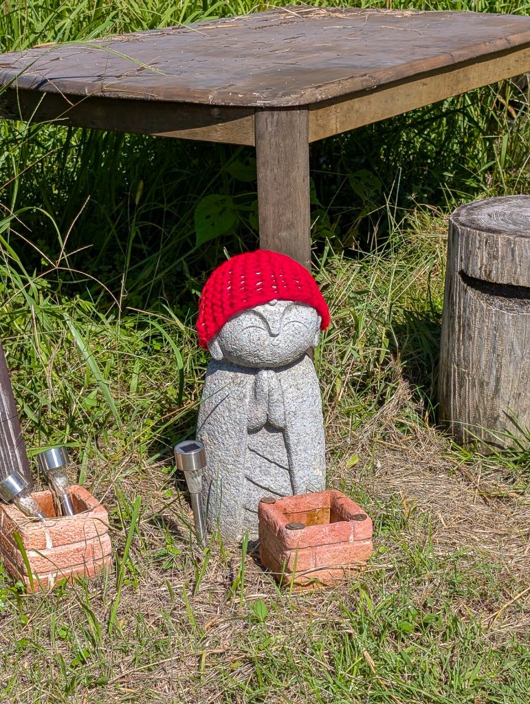 a small stone statue of Jizo Buddha wearing a red hat