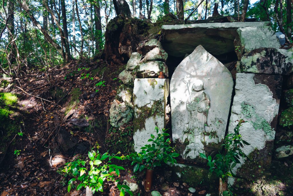 A white stone statue in the forest a Jizo shrine on the Kumano Kodo