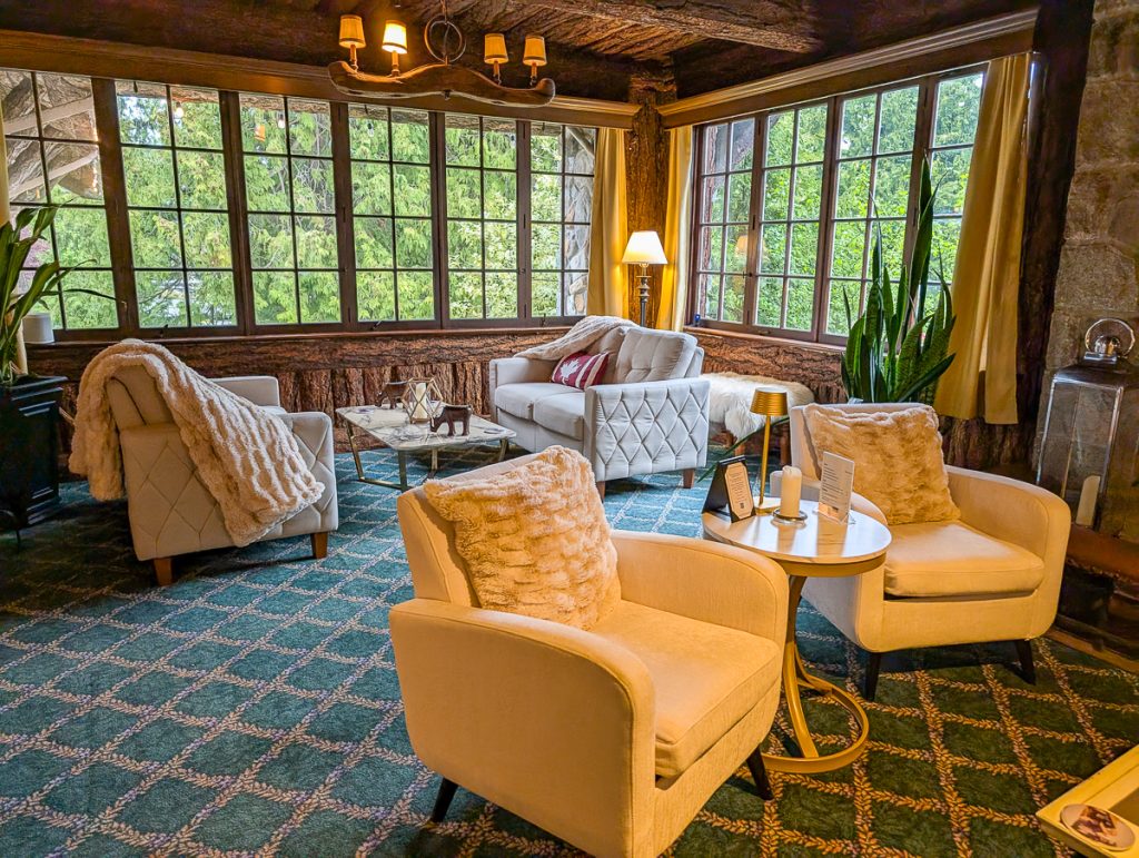 A cozy lounge with comfy chairs on carpet and big wooden windows looking out over greenery.