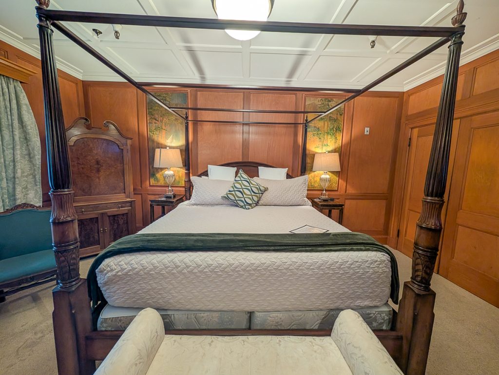 A four-poster bed inside a wood-panelled room with beautiful paintings on either side of the bed.