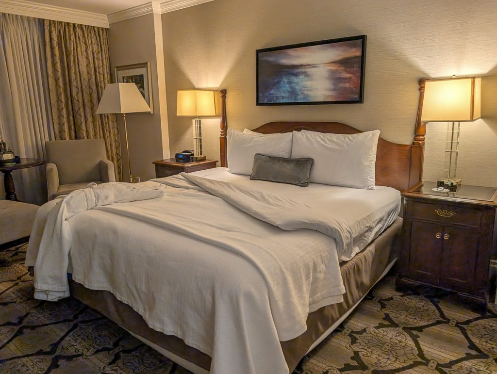 A comfy-looking bed in a hotel room with patterned carpet and square lamps on the side tables.