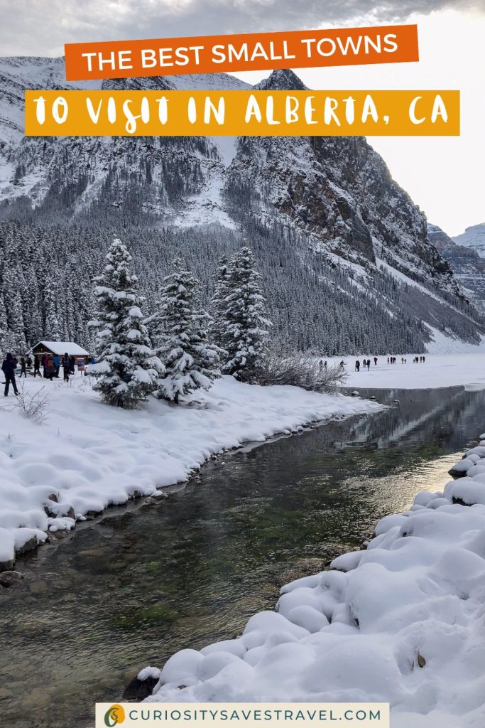 A snowy river with people and a small wooden building on the banks and a mountain in the background with text on top that says "The best small towns to visit in Alberta, CA."
