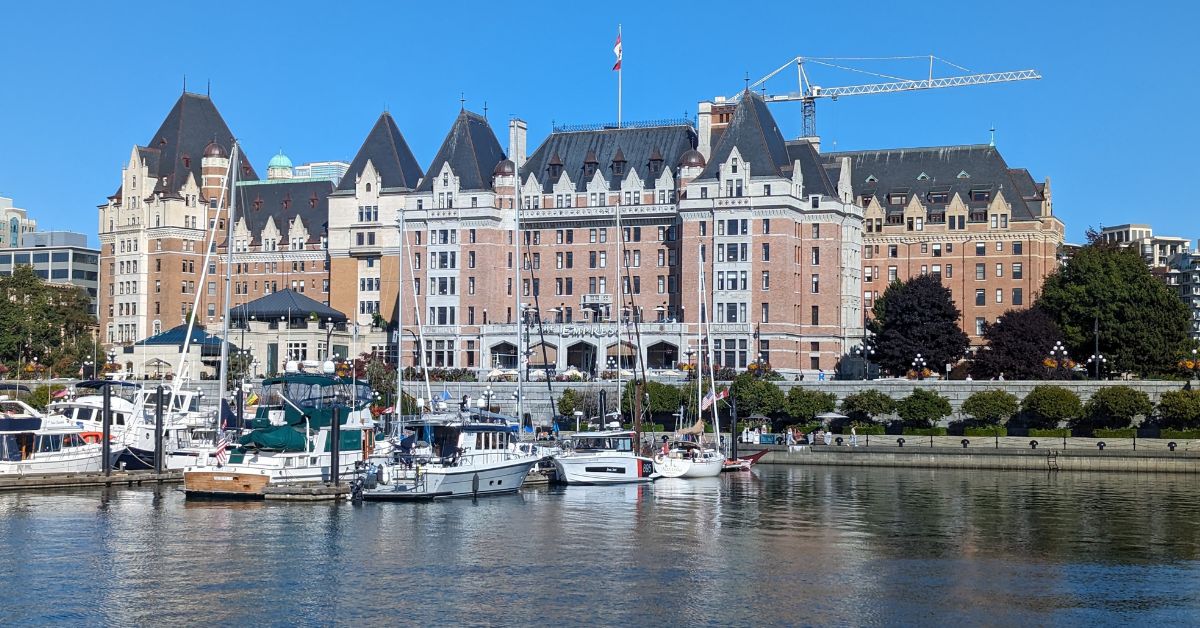 A grand stone building next to water with lots of yachts moored in front, as seen from the water.