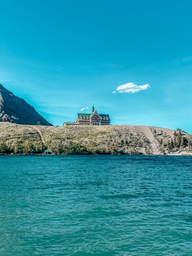 A photo of a hotel on an outcropping of land with a bright blue sky above and bright blue water in front.