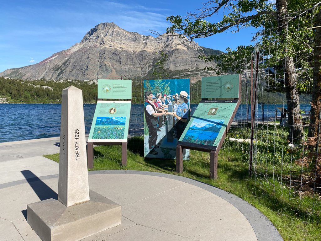 A cement monment with "Treaty 1925" carved into next to information panels beside a lake with a mountain in the background.