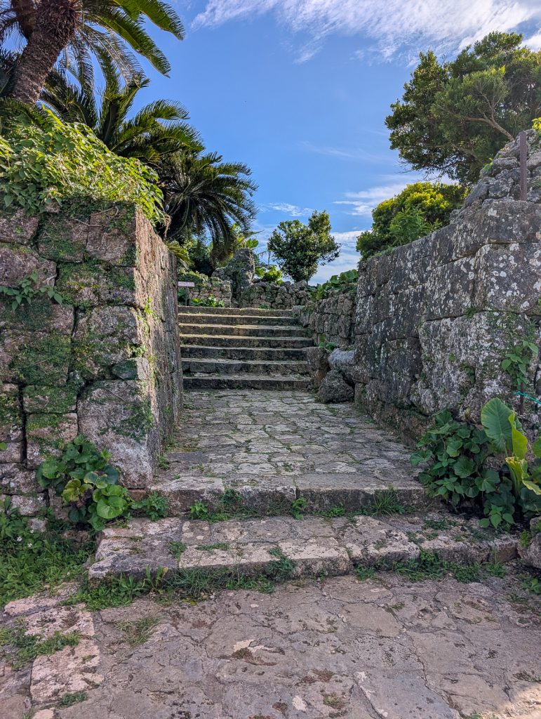 Some stone steps surrounded by short stone walls with trees growing behind and blue sky above.