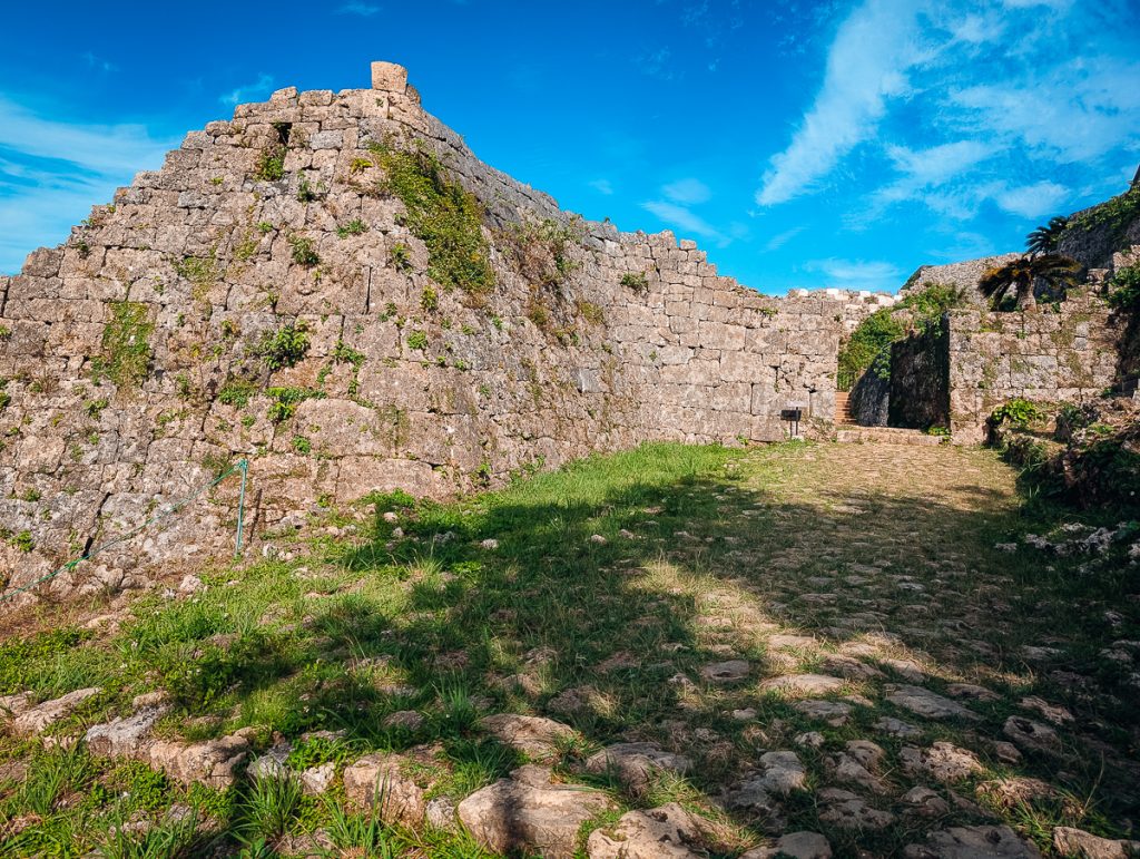 The remains of a stone structure next to an overgrown path with blue sky above.