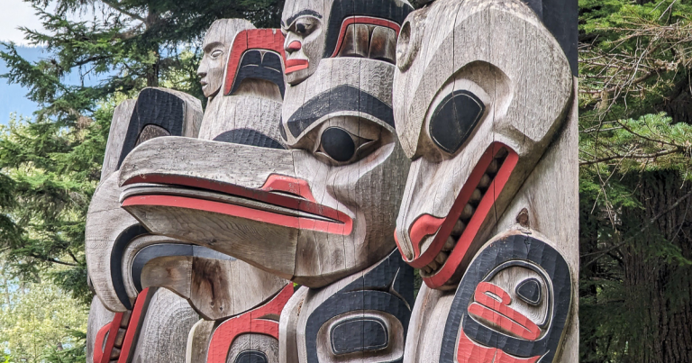 Four carved clan poles showing different animals and made of wood. The best Indigenous experiences to have across British Columbia