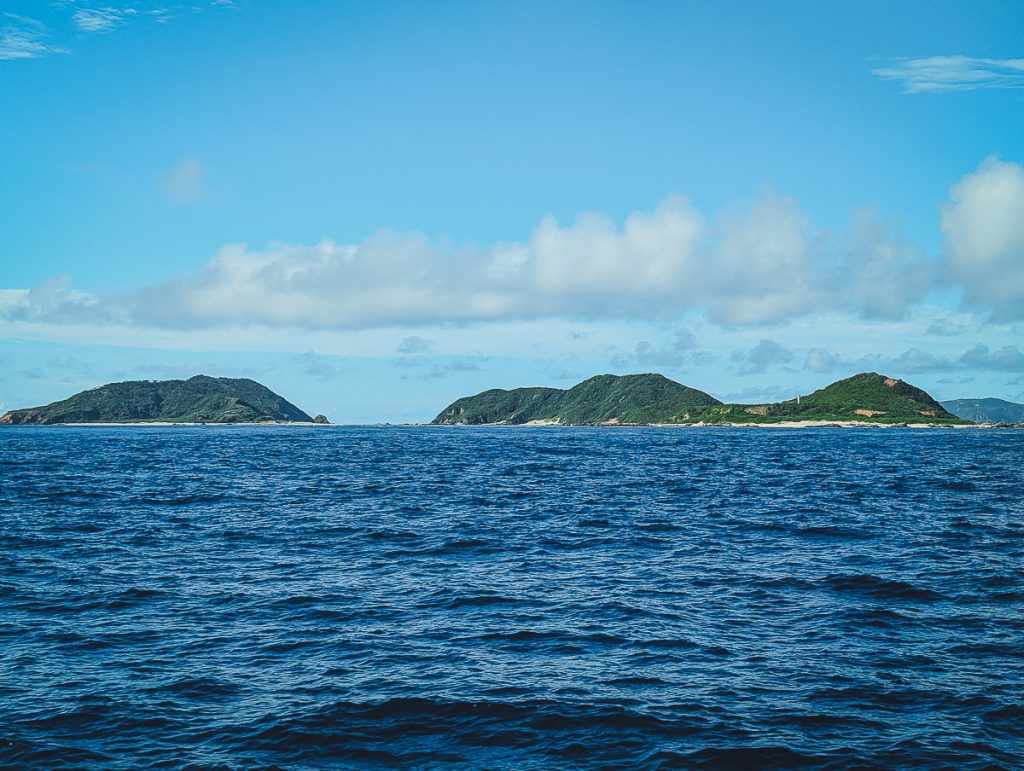 Small, forested islands in deep blue water with light blue skies above.
