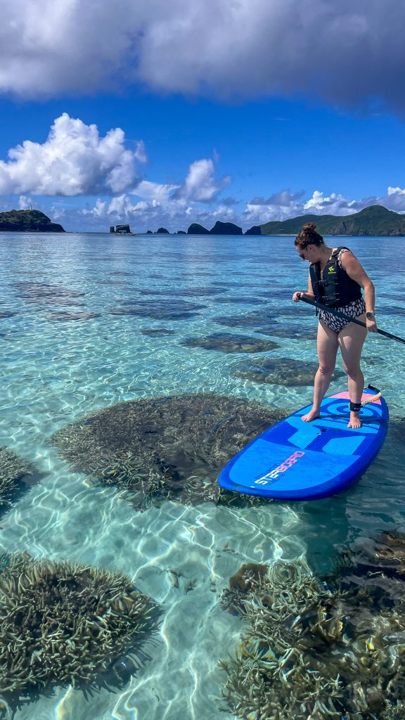Susanna stands on a SUP board over a coral reef
