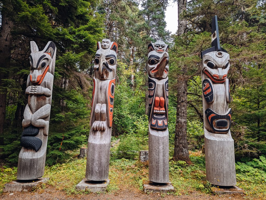 The four clan totem poles at Kitselas Canyon with pine trees behind them.