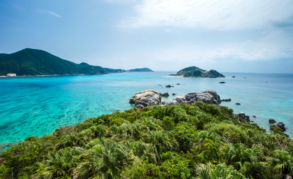 A tropical island with rocks pointing into bright blue water with more islands in the distance.